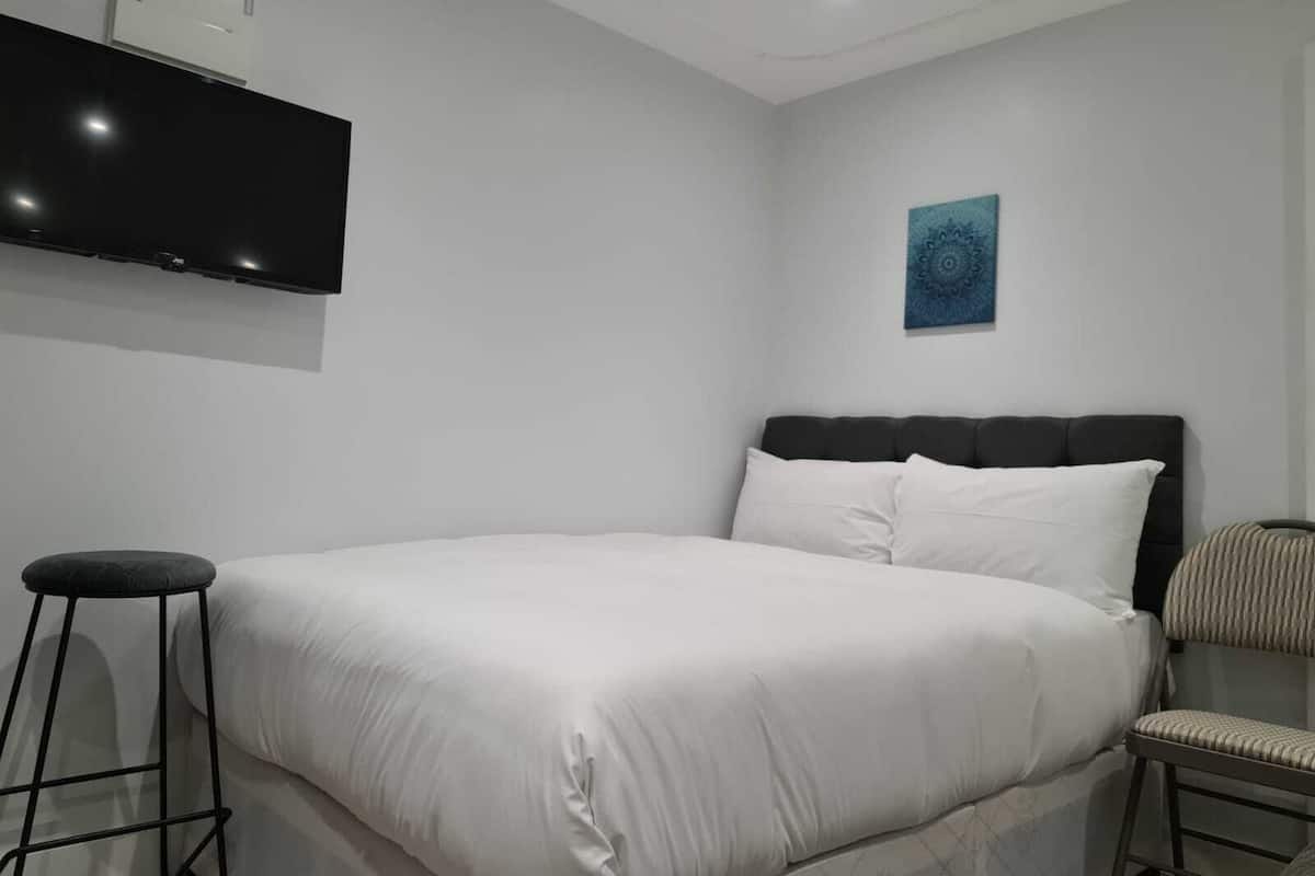 A modern bedroom with a large bed, a flat-screen TV mounted on the wall, and a small stool.