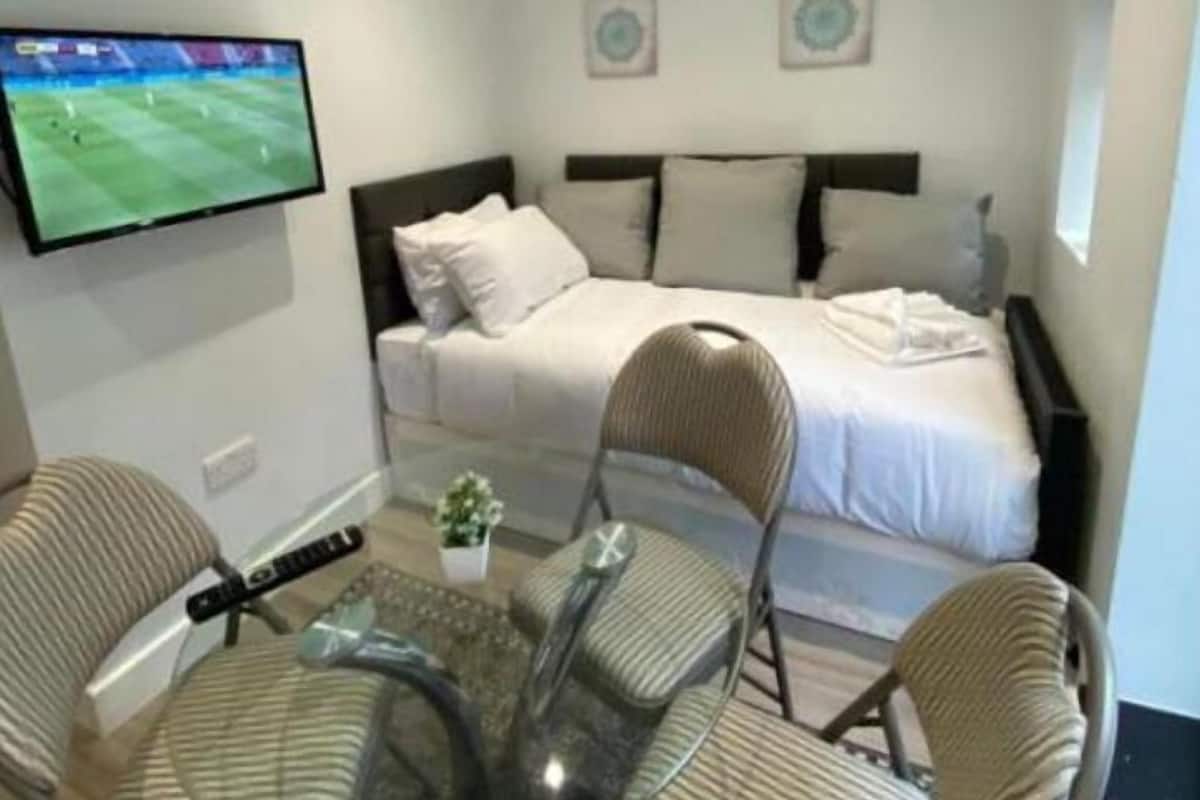 A hotel room with a bed, a TV mounted on the wall, a glass table with chairs, and a small plant.