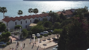 A coastal building with a red-tiled roof, surrounded by palm trees and parked cars. - Konak Hotel (Alanya)