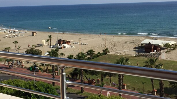 A beach with a clear view of the ocean, palm trees, and a few beach umbrellas. - Konak Hotel (Alanya)