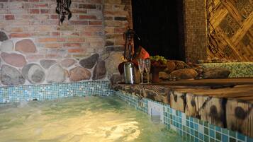 Un jacuzzi con borde de azulejos, pared de ladrillo y banco de madera.
