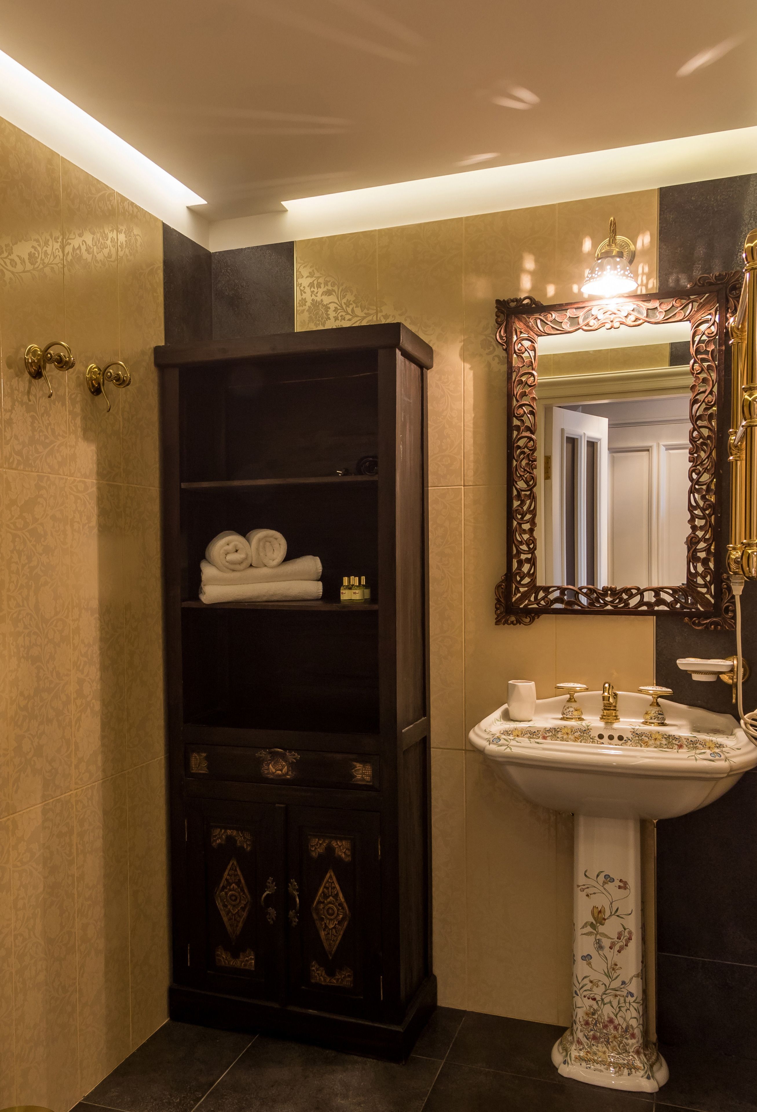 A bathroom with a dark wooden cabinet, a white pedestal sink, and a large ornate mirror.