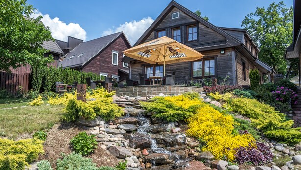 A wooden house with a patio, a small waterfall, and colorful garden beds. - Argo Trakai (Trakai)