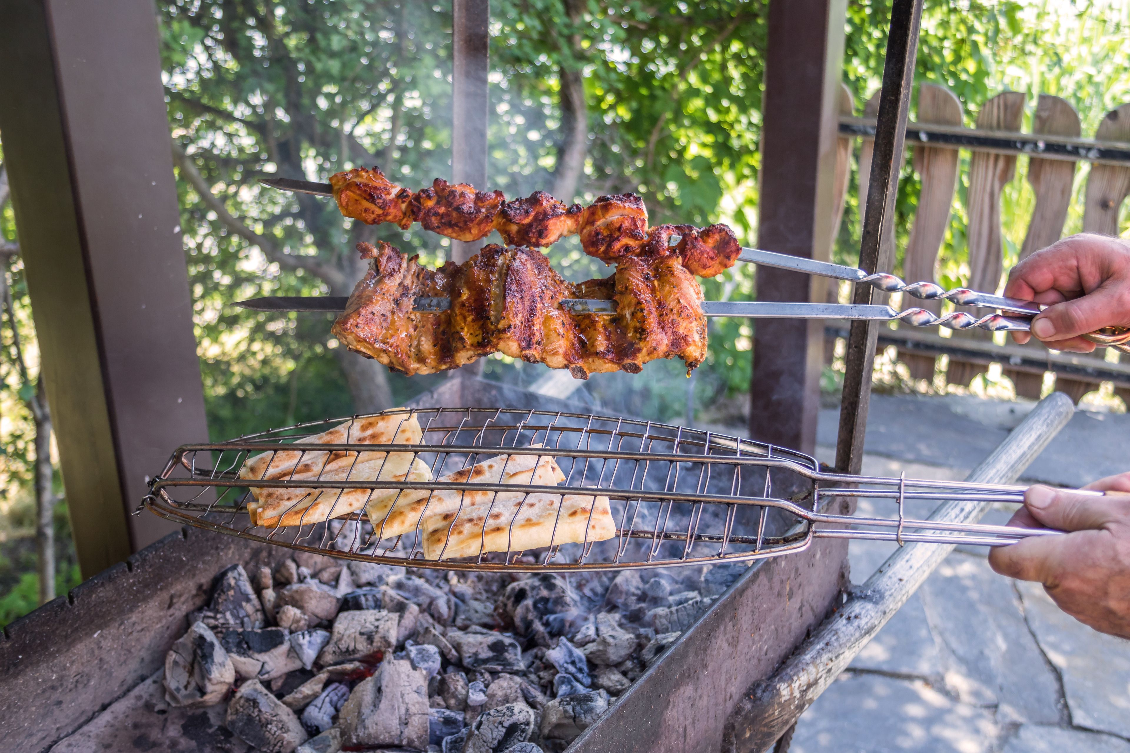 A grill with skewers of meat and flatbread being cooked outdoors.