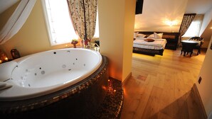 A room with a large bathtub, a bed with pillows, and a wooden floor. - Argo Trakai (Trakai)