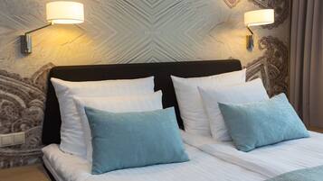 Una cama bien tendida con almohadas blancas y azul claro, cabecera oscura y dos lámparas fijadas a la pared.