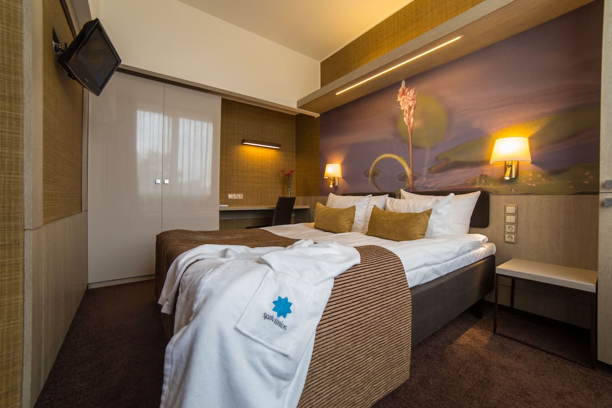 A hotel room with a bed, a TV mounted on the wall, a desk with a chair, and a painting on the wall.