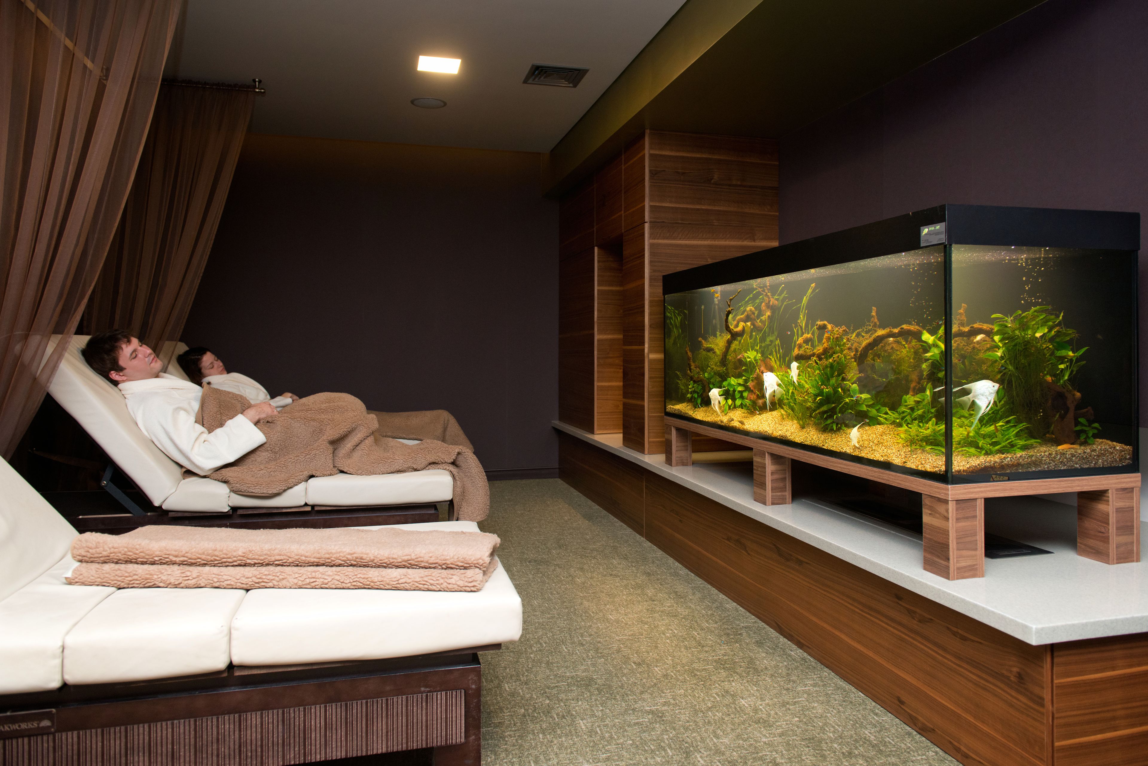 Une salle de spa dotée d’un grand aquarium, d’une table de massage et d’un mur recouvert de panneaux en bois.