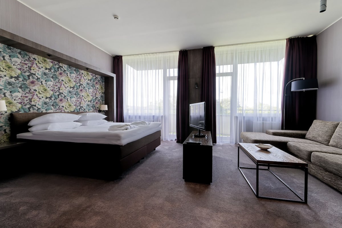 A hotel room with a bed, a sofa, a TV, and a coffee table.