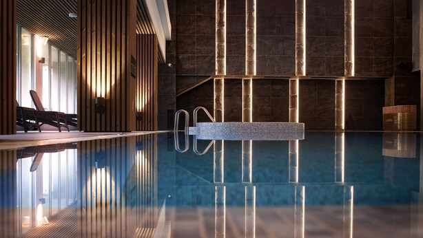 A modern indoor pool area with a clear pool, wooden slats, and a stone wall. - SPA VILNIUS Druskininkai (Druskininkai)