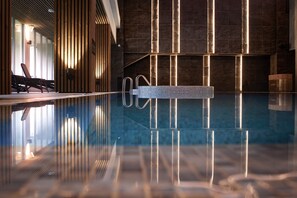 A modern indoor pool area with a clear pool, wooden slats, and a stone wall. - SPA VILNIUS Druskininkai (Druskininkai)