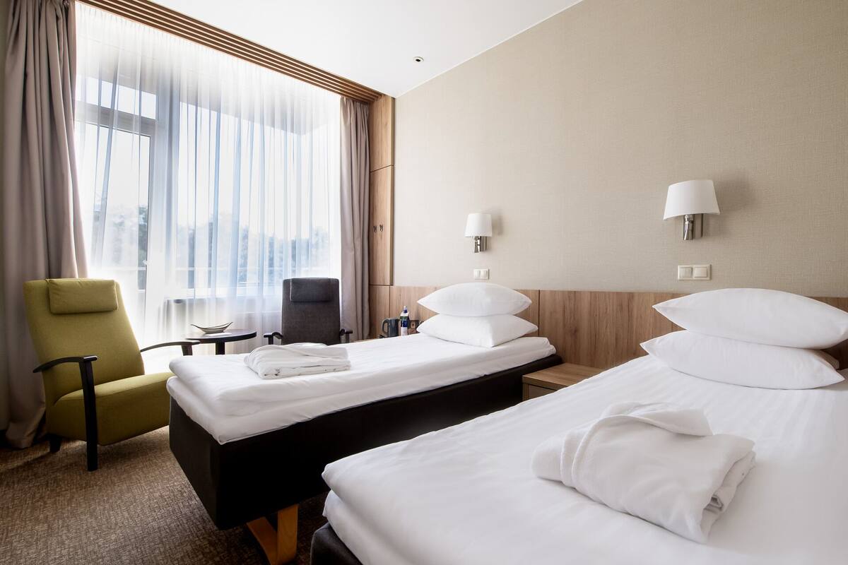A hotel room with two beds, a desk, a chair, and a view of the city.