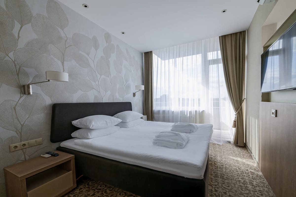 A hotel room with a large bed, a TV, a bedside table, and a window with curtains.