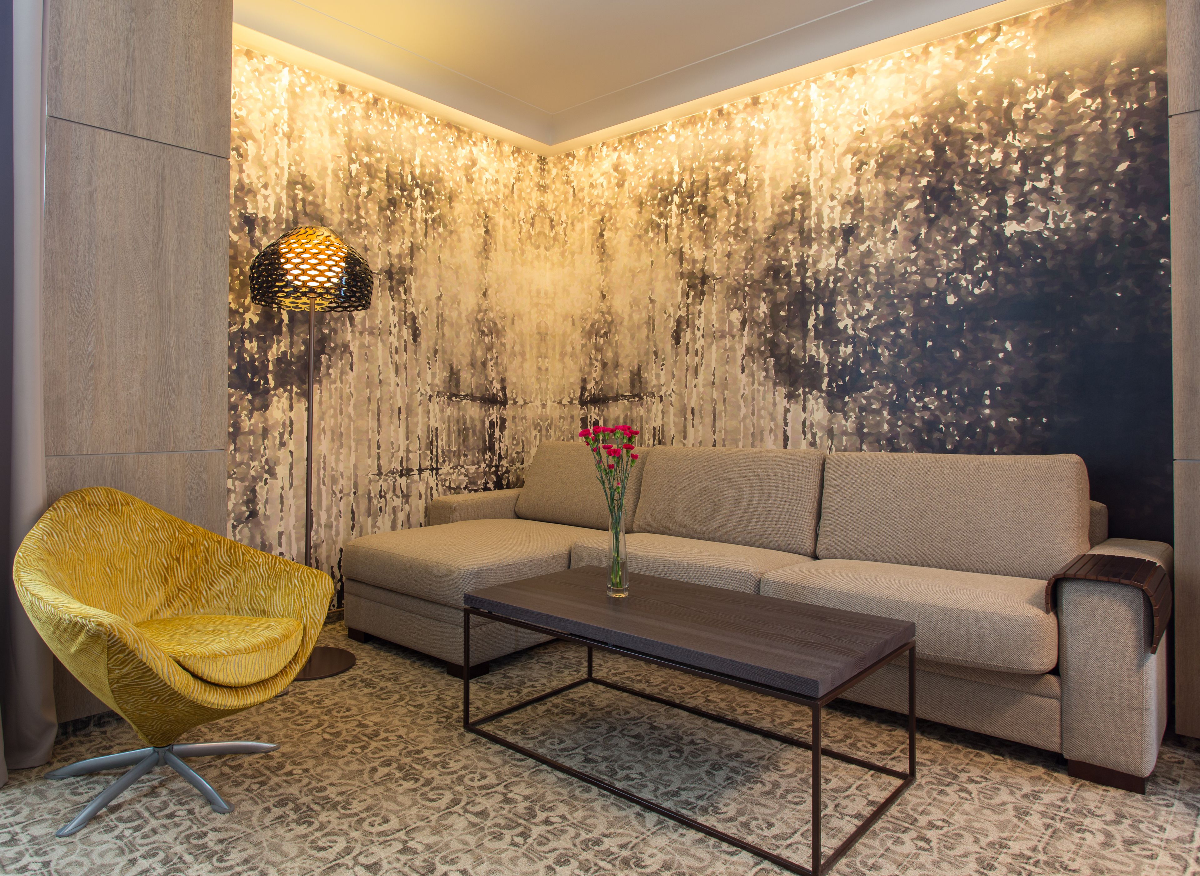 Un salon moderne avec un canapé à motifs, un fauteuil jaune, une table basse et un mur décoratif présentant un motif texturé.