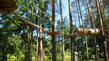 Un puente colgante en un bosque con plataformas de madera y una estructura cilíndrica.