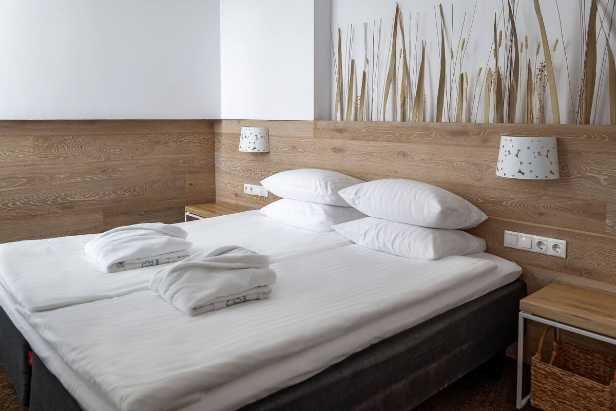 A neatly made bed with white linens and pillows, a wooden headboard, and a wall-mounted lamp with a geometric pattern.