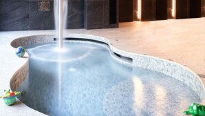A hot tub with a waterfall feature, surrounded by dark stone walls and a tiled floor. - SPA VILNIUS Druskininkai (Druskininkai)
