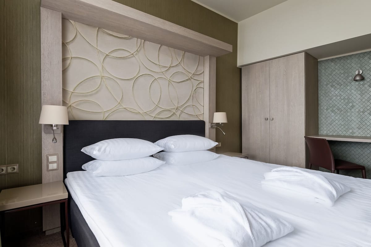 A hotel room with a bed, two bedside lamps, a desk, and a wardrobe.