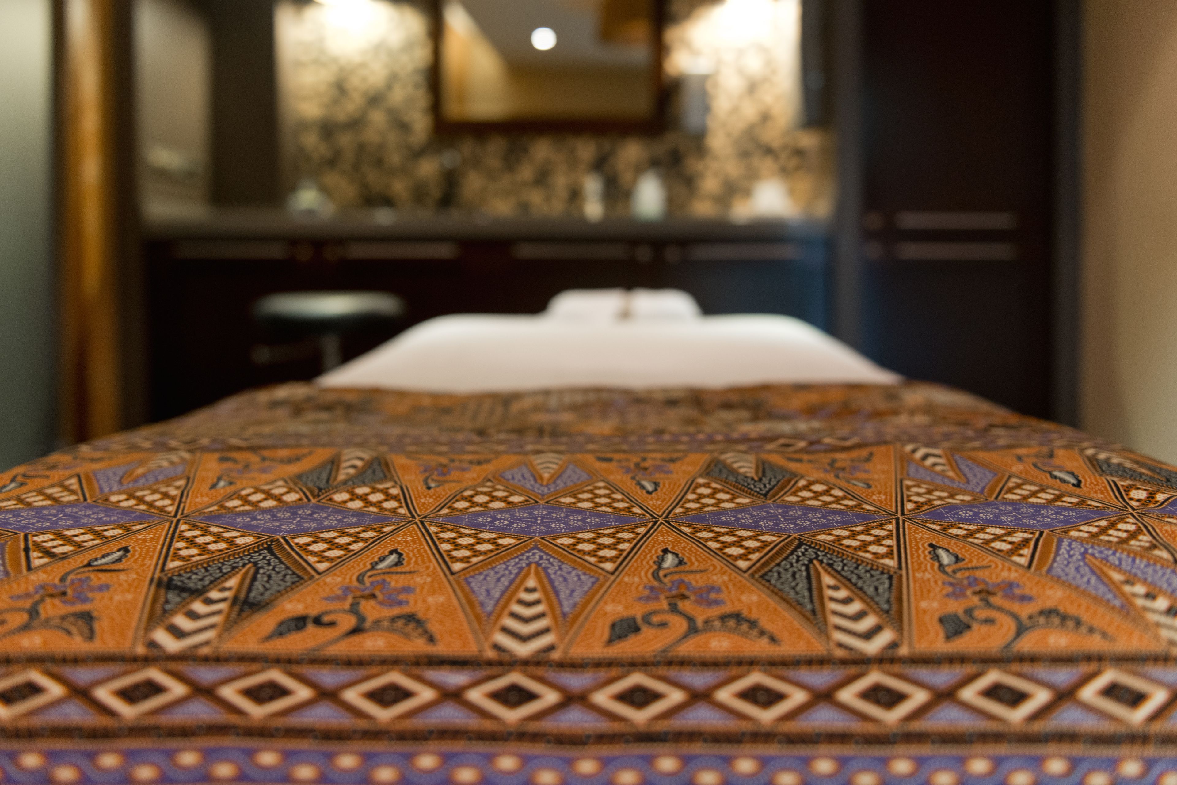 Un lit avec une couvre-lit à motifs, un oreiller blanc et une tête de lit.