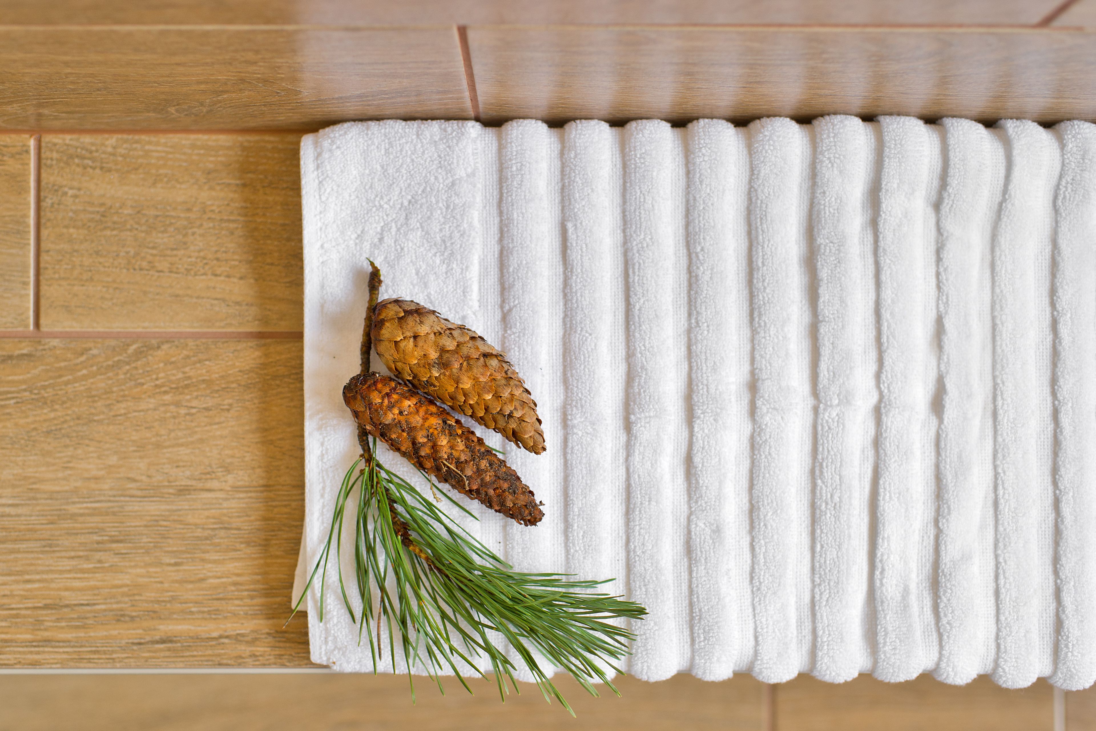 Une serviette blanche ornée de pommes de pin et d’aiguilles de pin, posée sur un plancher en bois.
