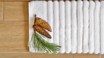 Une serviette blanche ornée de pommes de pin et d’aiguilles de pin, posée sur un plancher en bois.