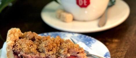 Une part de tarte sur une assiette, accompagnée d’une cuillère, une tasse de café avec un logo rouge et une soucoupe sur une table en bois.