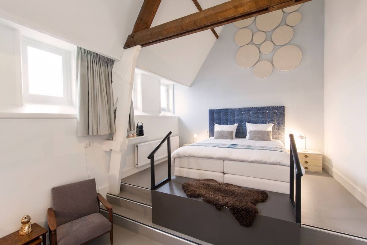 Une chambre à coucher avec un lit, une chaise, un escalier et une vue sur l’extérieur.