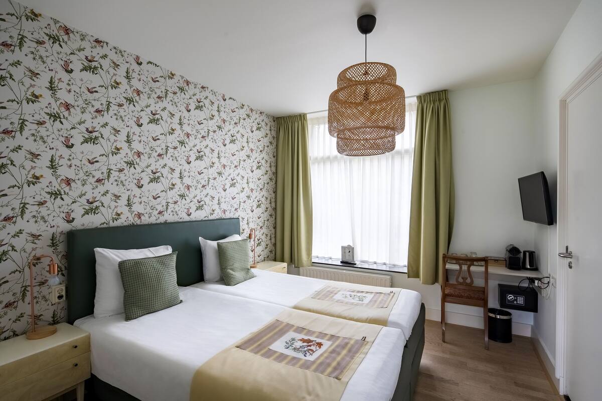 Une chambre d’hôtel avec deux lits, un bureau, une télévision et une fenêtre avec des rideaux.