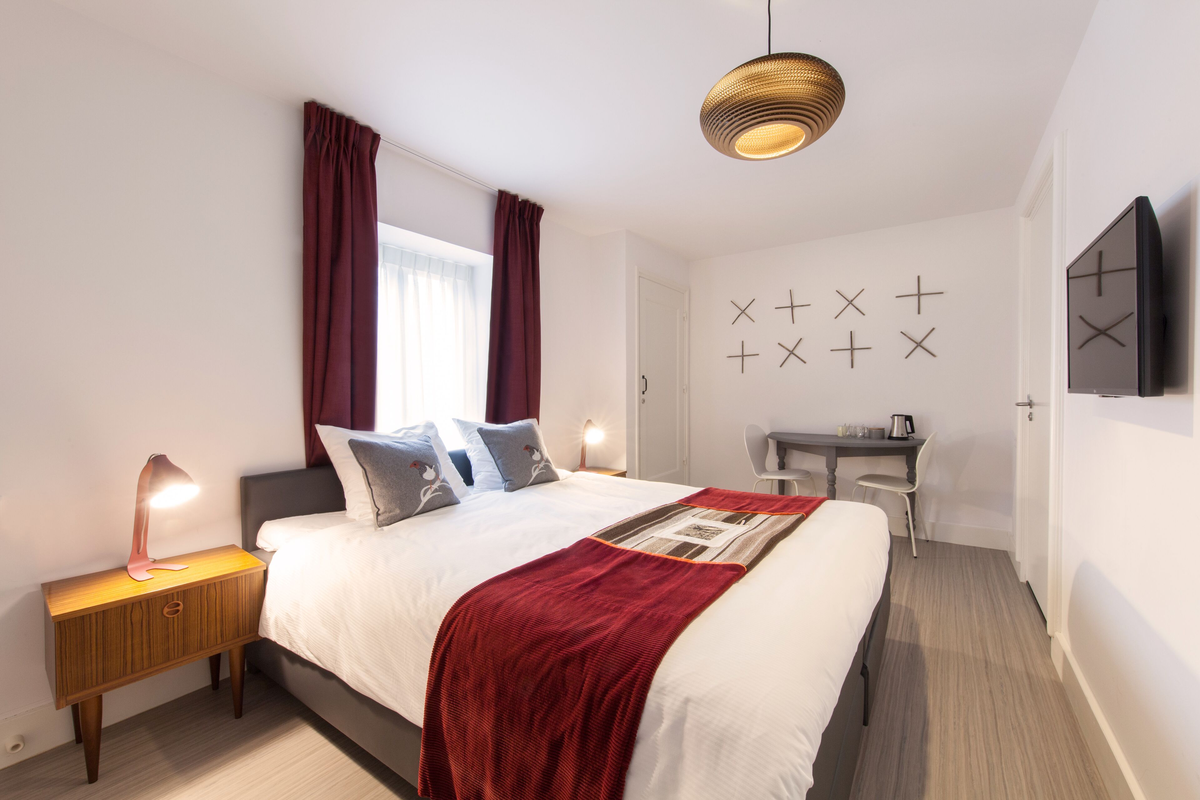 A modern bedroom with a bed, bedside lamp, desk, and a wall-mounted TV.