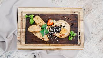 A wooden board with food items including bread, a strawberry, and a cheese wheel, placed on a speckled surface.