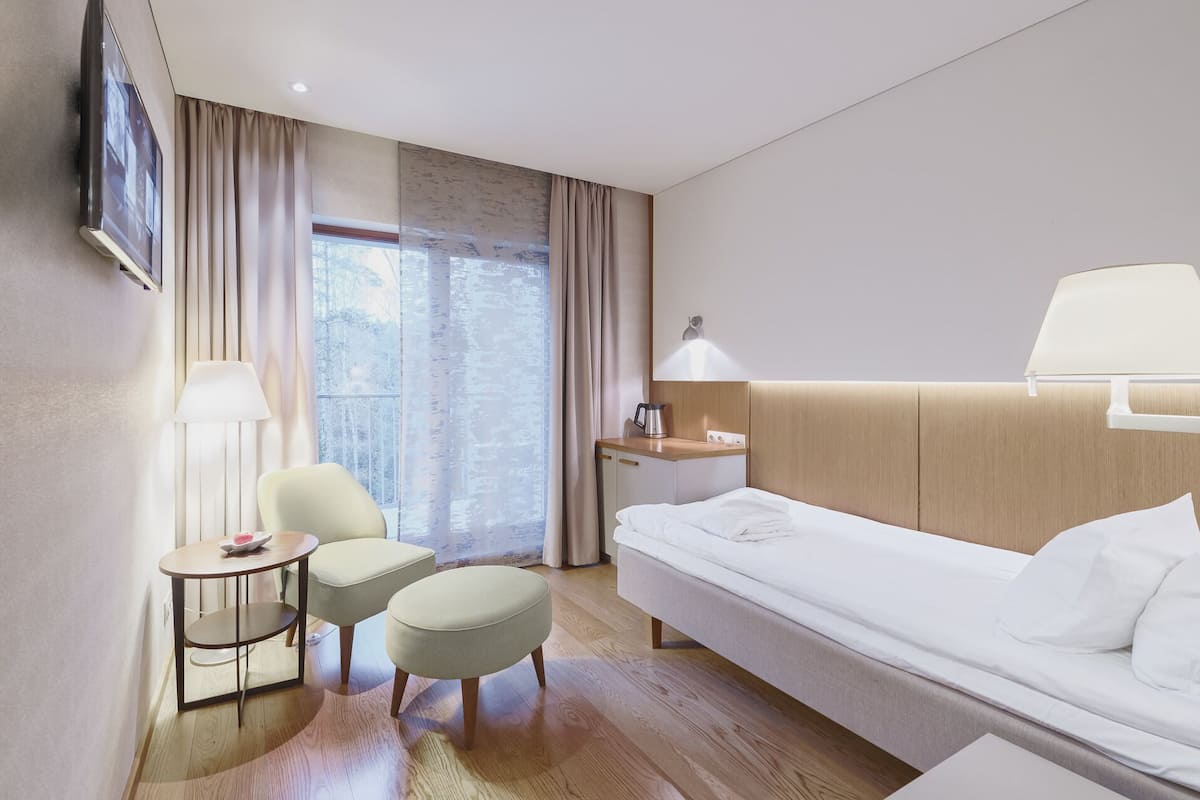Ein Hotelzimmer mit einem Bett, einem Schreibtisch mit Lampe, zwei Stühlen, einem kleinen Tisch mit Teller und einem an der Wand befestigten Fernseher.