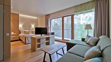 A modern hotel room with a bed, a TV, a sofa, and a balcony with a view of trees.