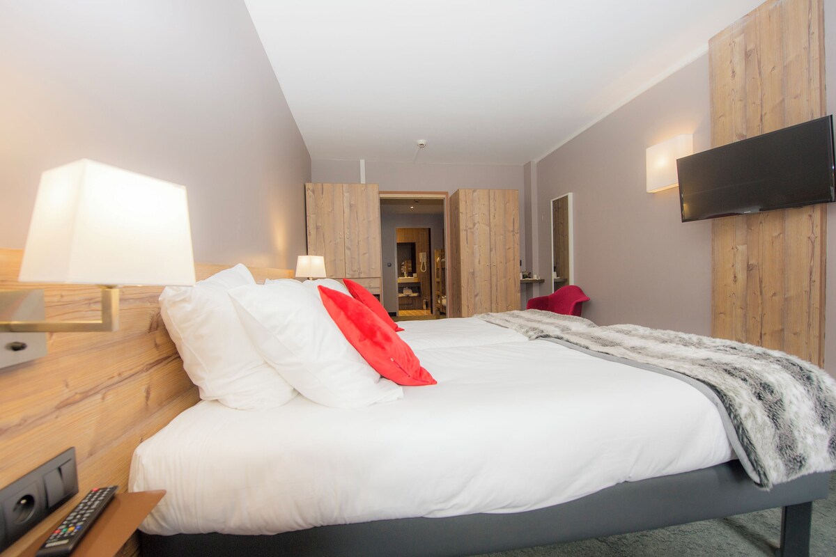 A hotel room with a bed, a TV mounted on the wall, a lamp, and a remote control on the side table.