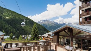A mountain lodge with a wooden deck, outdoor seating, and a view of snow-capped mountains. - SOWELL Family Valfréjus (Modane)