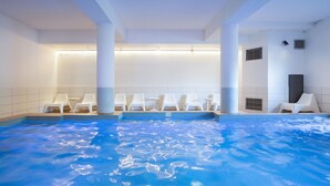 A swimming pool with white chairs around it, a ceiling with lights, and a tiled wall. - SOWELL Family Valfréjus (Modane)