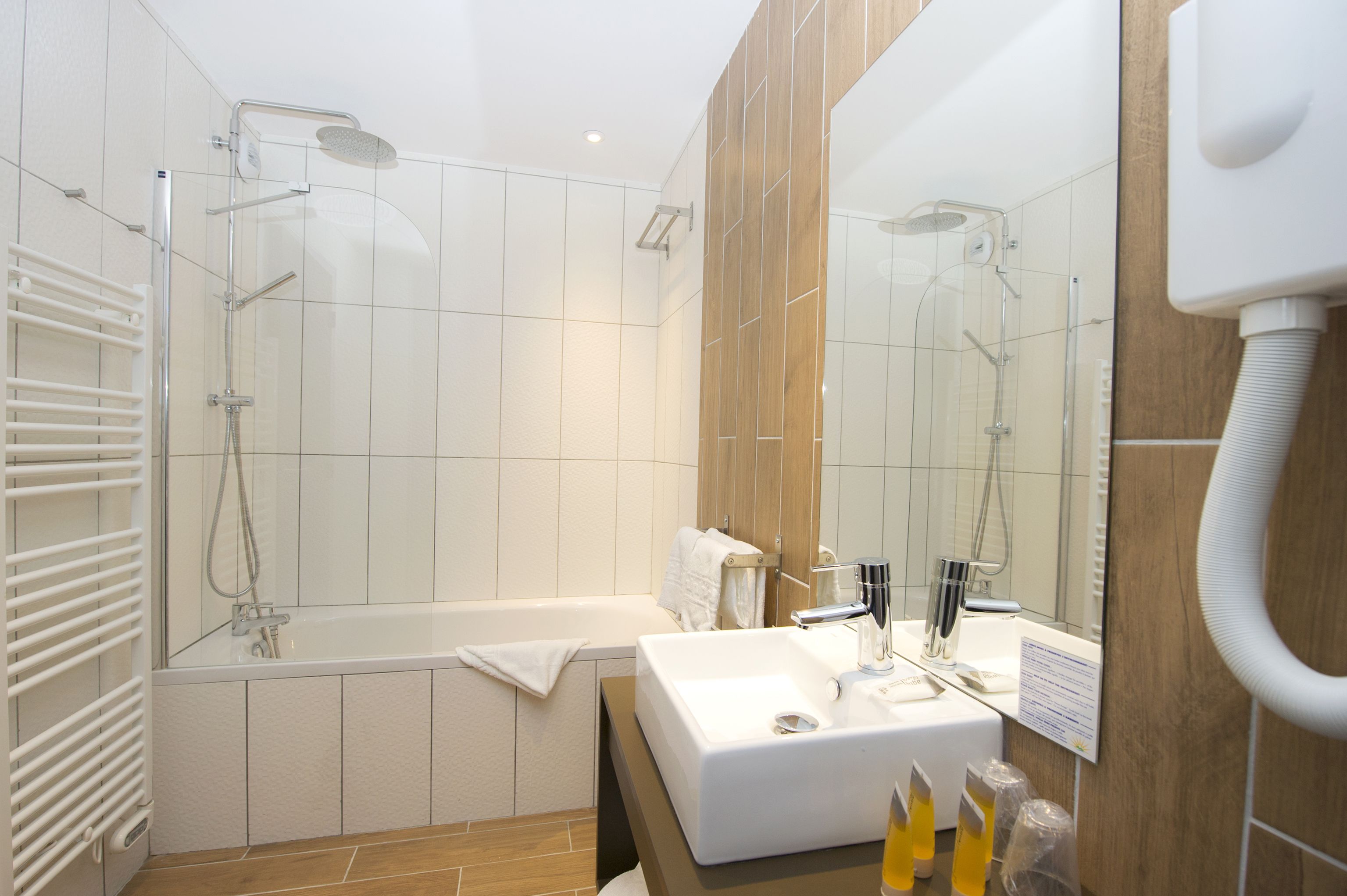 A modern bathroom with a glass-enclosed shower, a white bathtub, and a sink with a mirror.
