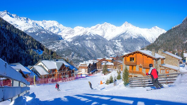 A ski resort with snow-covered mountains in the background, wooden buildings with balconies, and a clear blue sky. - SOWELL Family Valfréjus (Modane)