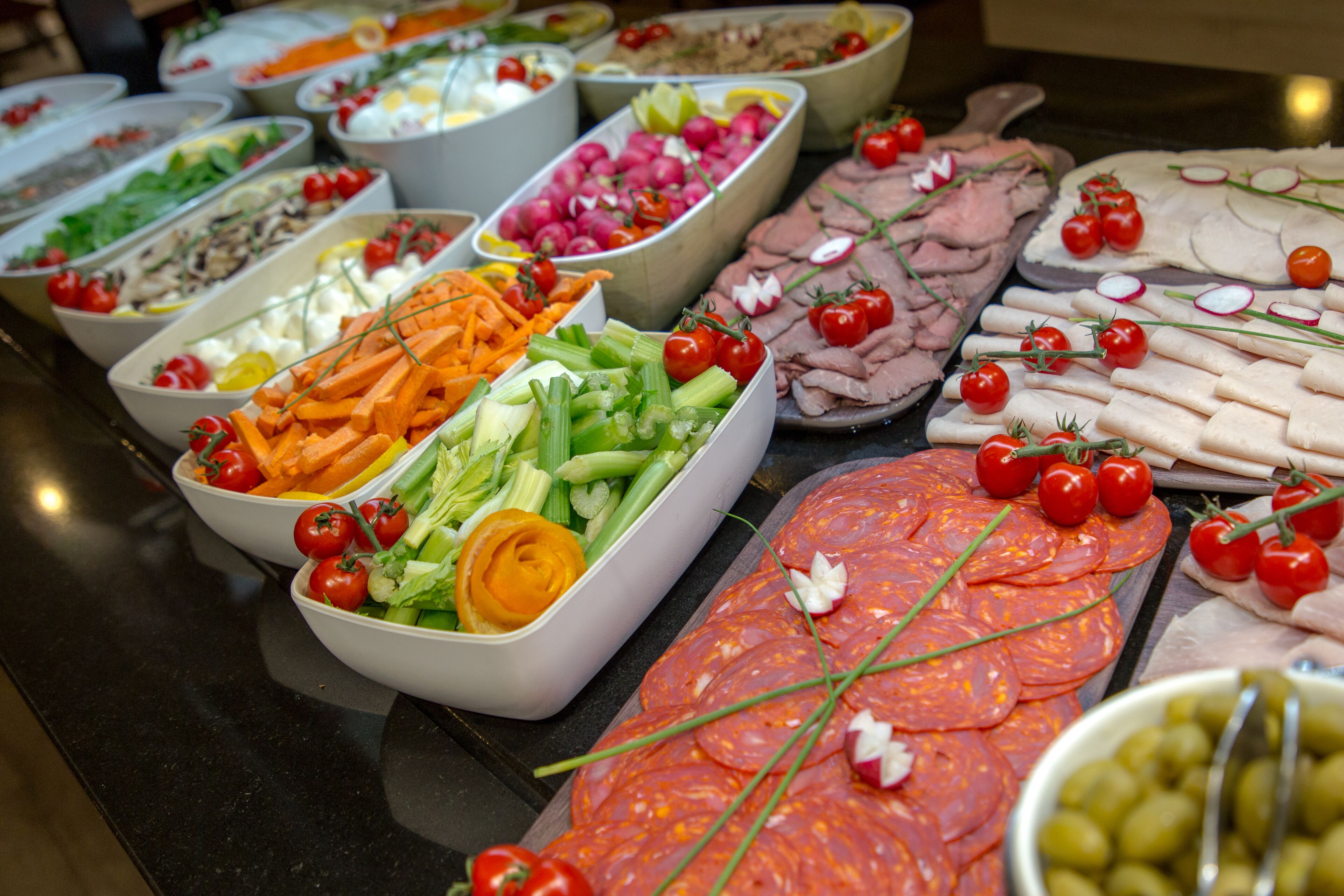 Un bufé con diversas opciones de comida, incluyendo carnes, quesos y verduras.