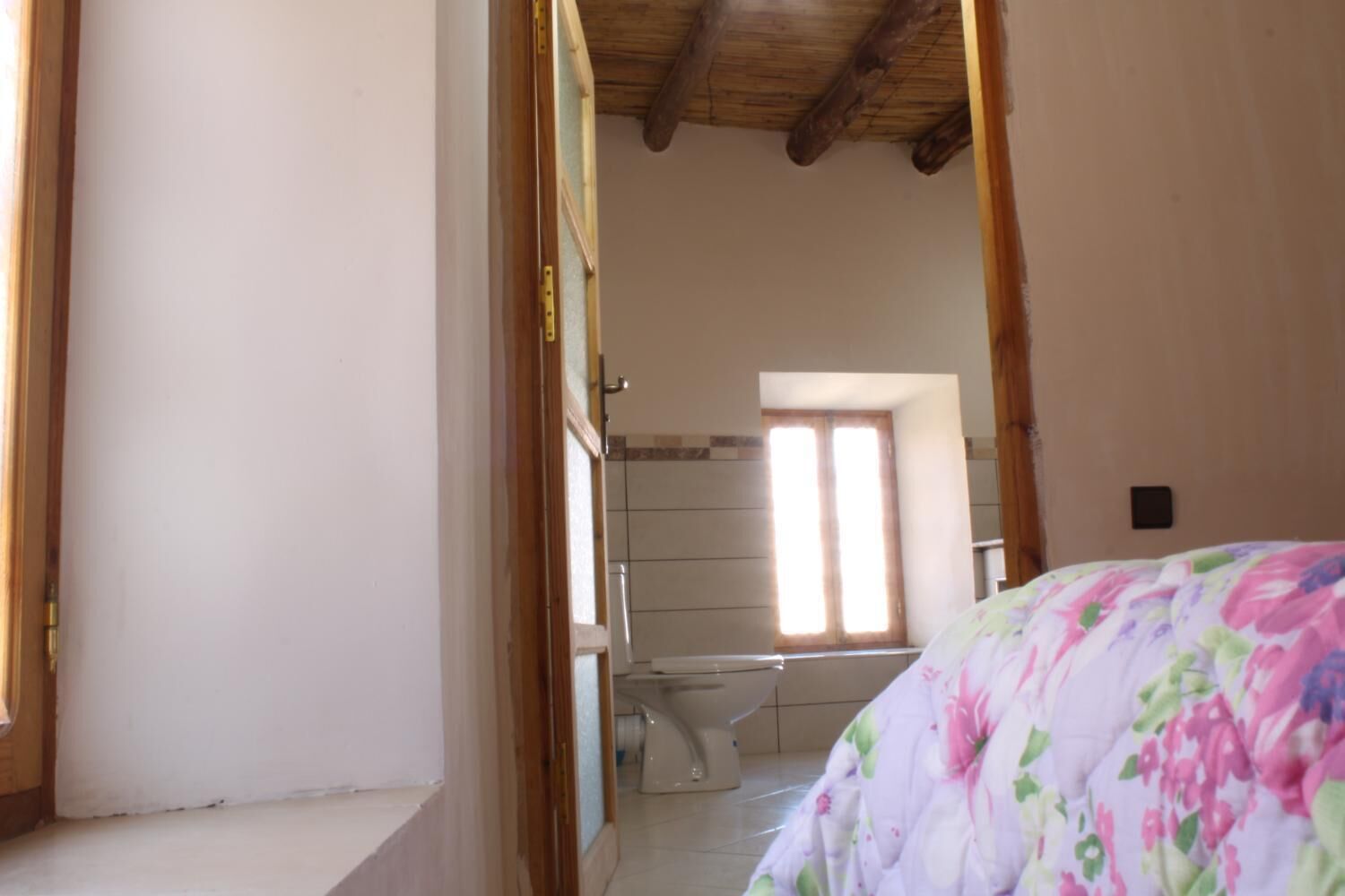 A bedroom with a bed, a window, and a bathroom with a toilet and shower.
