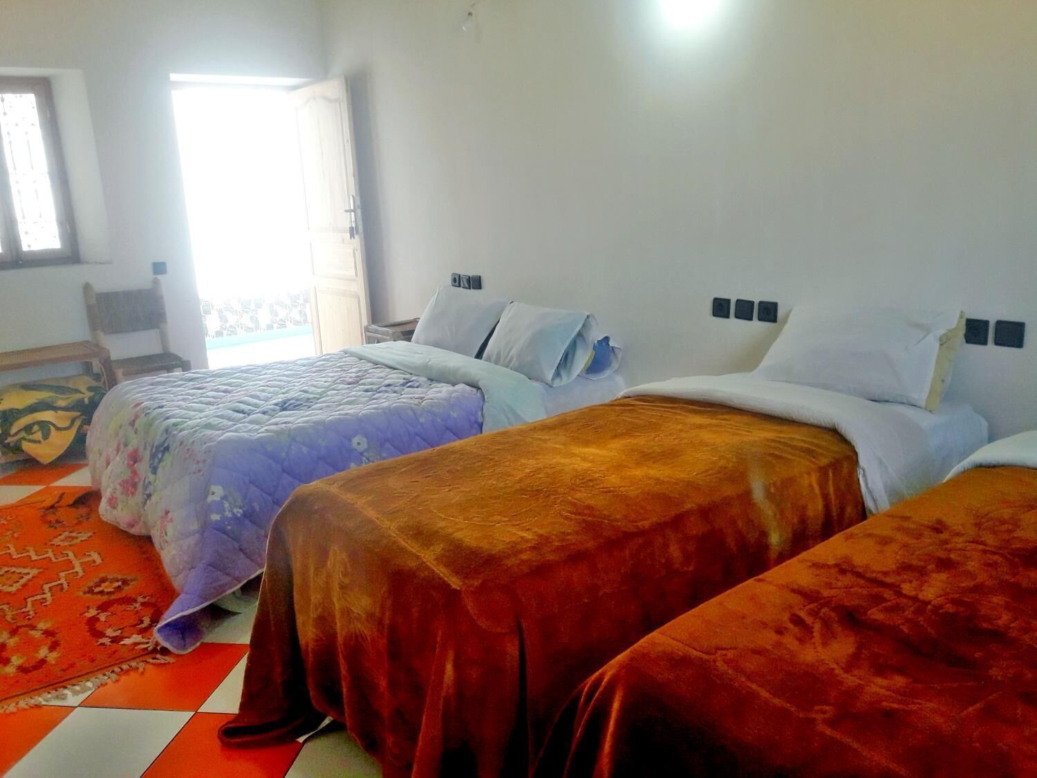 A hotel room with three beds, a window with a view, a chair, and a patterned rug.