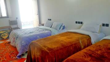 A hotel room with three beds, a window with a view, a chair, and a patterned rug.