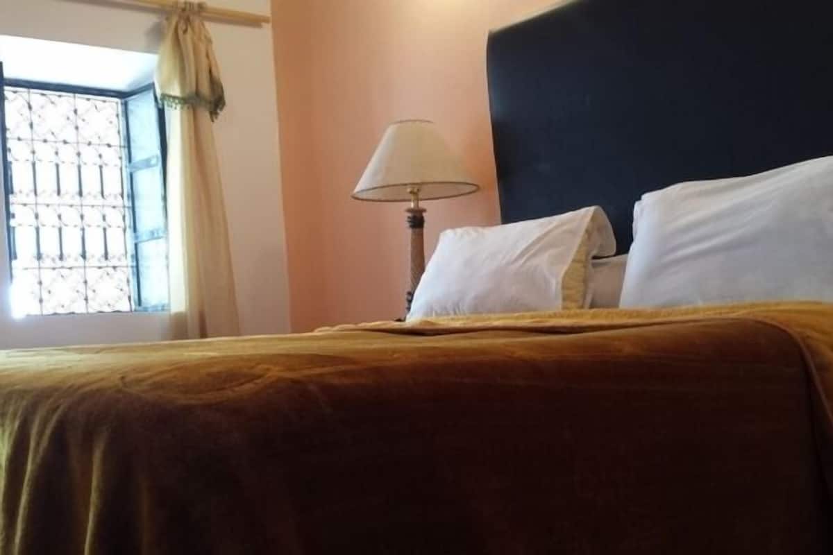 Hotellihuone, jossa on sänky, lamppu ja ikkuna, jossa on verhot.
