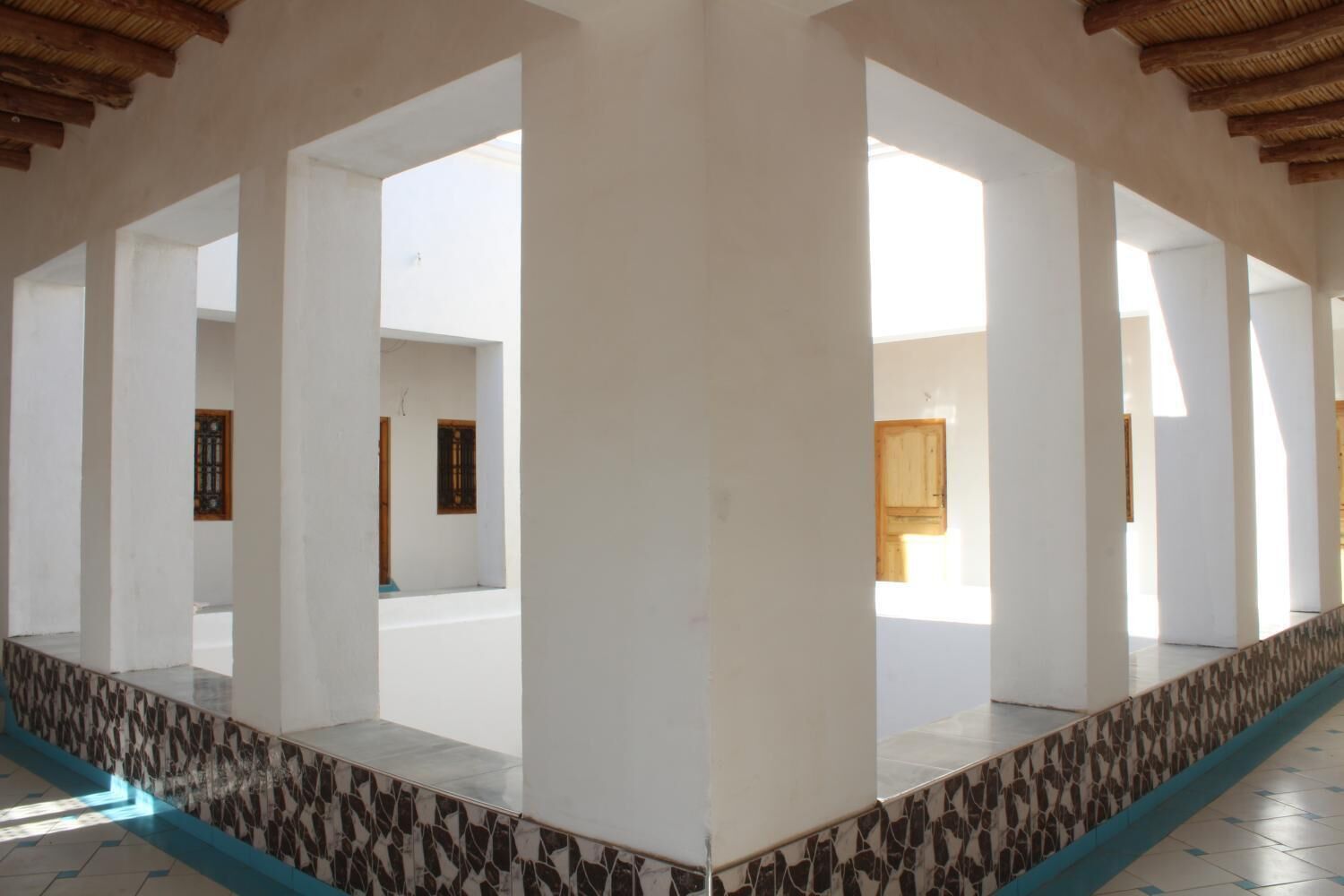 An interior corridor with white walls, a tiled floor, and a patterned border.