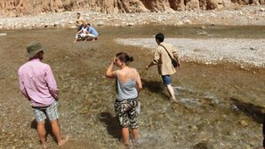 Un grupo de personas caminando por un río poco profundo con acantilados rocosos al fondo.