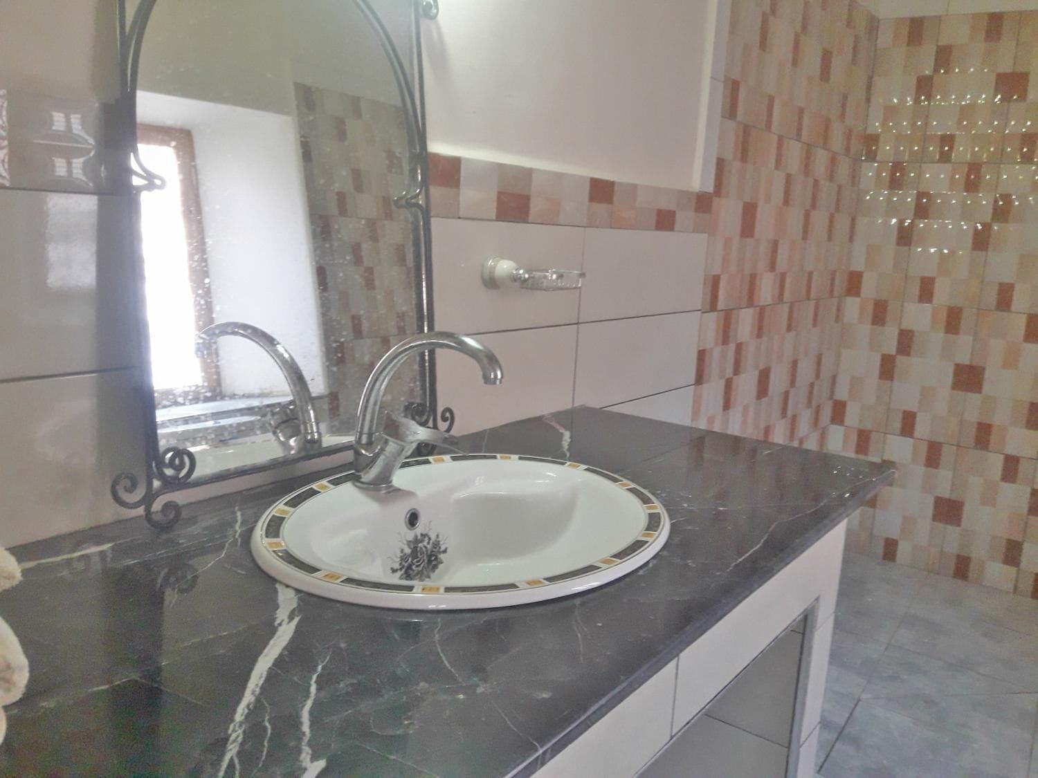 Une salle de bain avec un lavabo blanc, un miroir et des murs carrelés.