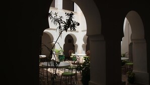Un patio al aire libre con mesas y sillas redondas, rodeado de arcos y plantas en macetas.