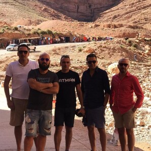 A group of people standing in a desert-like environment with rocky terrain and sparse vegetation.