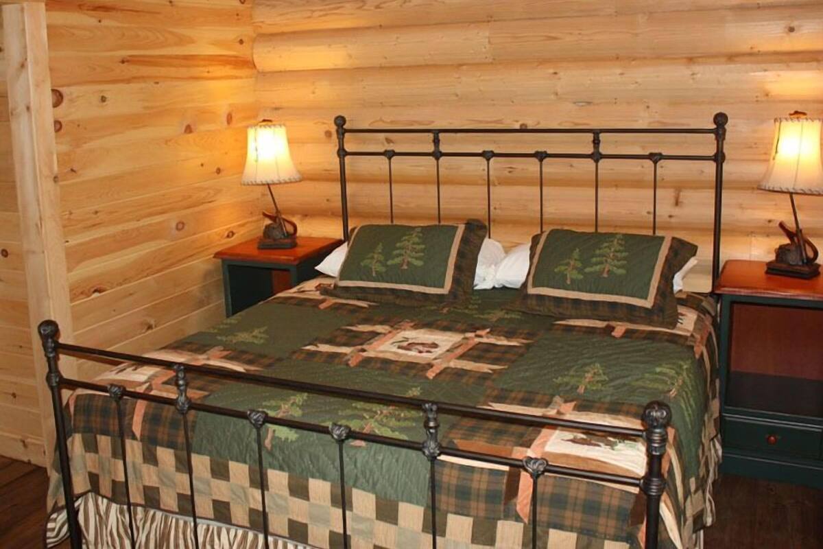 A wooden cabin-style bedroom with a metal bed frame, two bedside lamps, and a quilted bedspread.