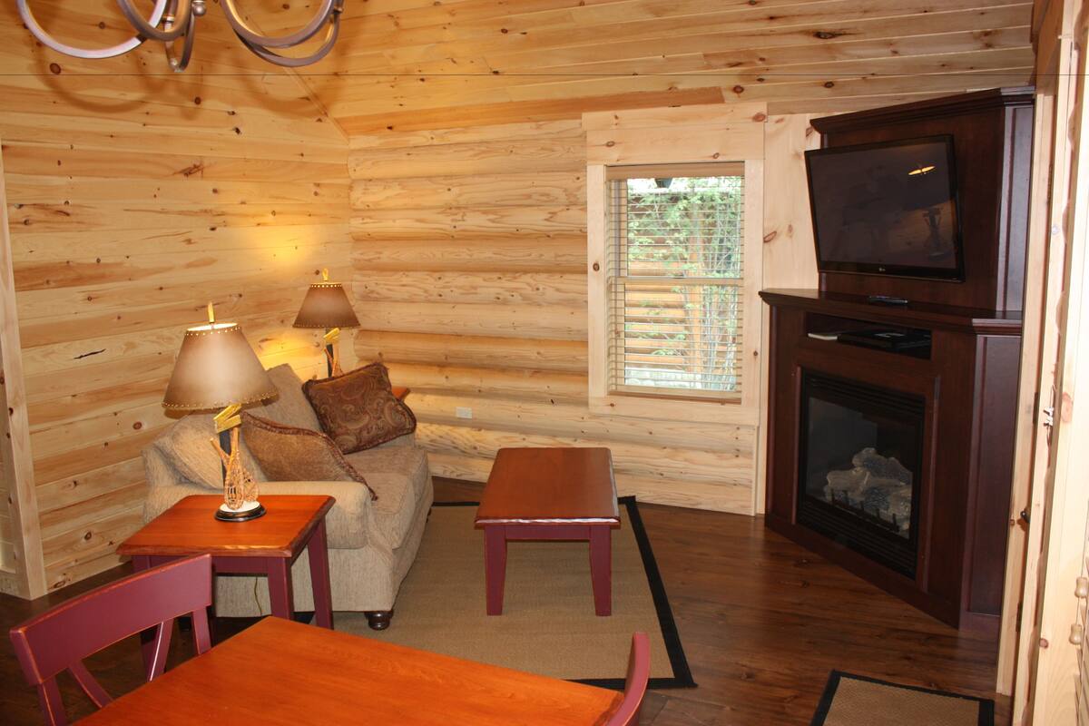 A log cabin interior with a sofa, two lamps, a television, and a fireplace.
