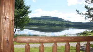 A wooden deck with a view of a calm lake and a forested hill in the background. - Lake Parlin Lodge & Cabins (Jackman)